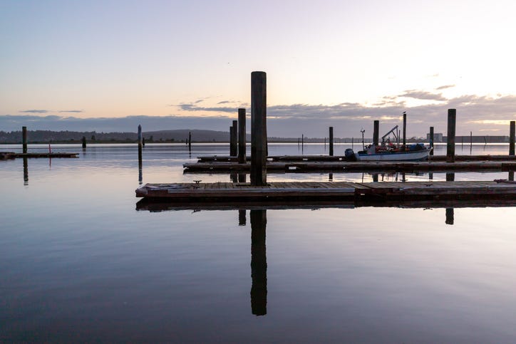 A line of boat launches and docks in still water. A fishing boat is docked at one in the background.