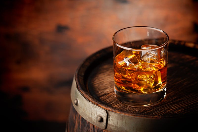 Glass of whiskey with ice cubes on the old barrel