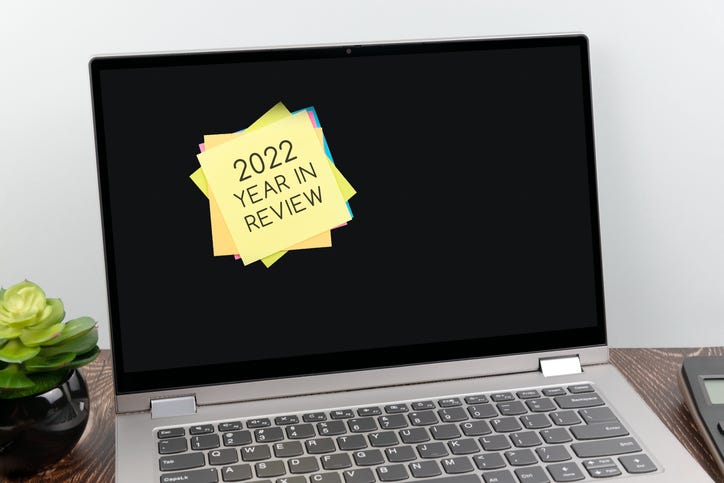 A laptop is open with a stack of multi-colored post-its stuck to the screen. The post-it on top reads "2022 Year in Review"