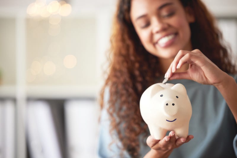 Person smiling as they put money in a piggy bank. 