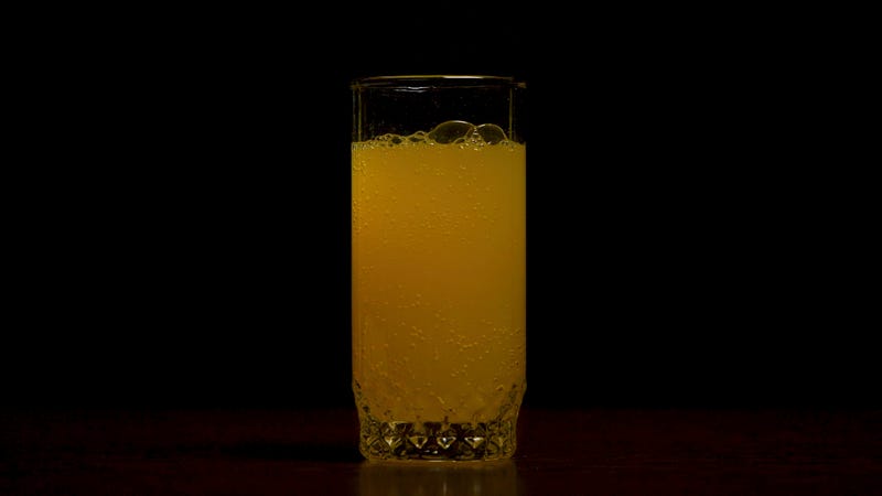 Orange soda large glass, overflowing glass of orange soda closeup with bubbles isolated on black background. Pouring Orange Drink. Slow Motion. Carbonated orange drink is poured into a glass. Pouring orange juice soda in glass in slow motion, black background