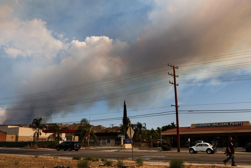 A pedestrian walks as smoke rises from the Fairview Fire on September 7, 2022 near Hemet, California.