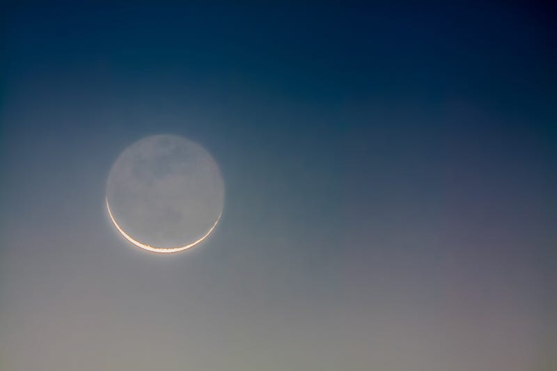 Crescent moon showing earthshine at sunrise