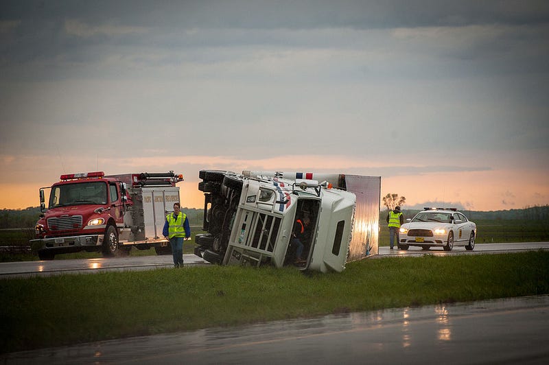 A semi-trailer truck on its side on the road, plus a fire truck.