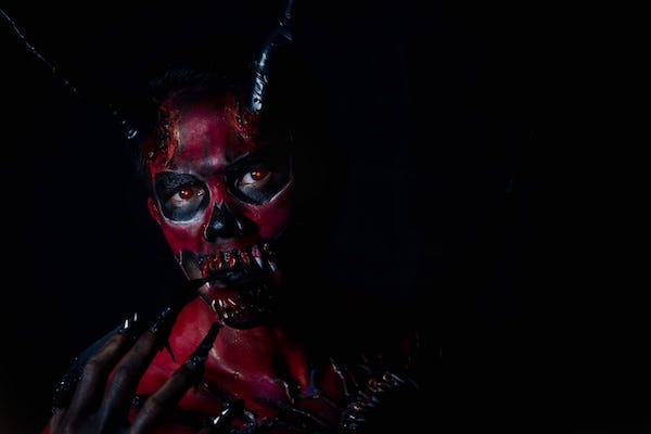 Man wearing a red, demon mask against black background