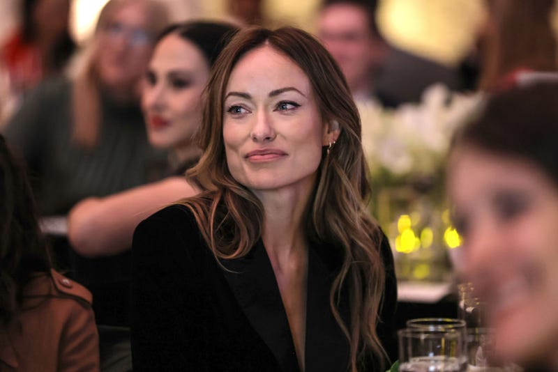 Olivia Wilde seated at table smiling with mouth closed