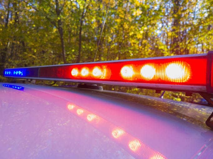 Police car with lights on along a tree-lined road