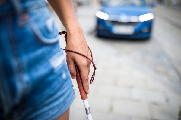 Blind woman walking with a cane in front of a car