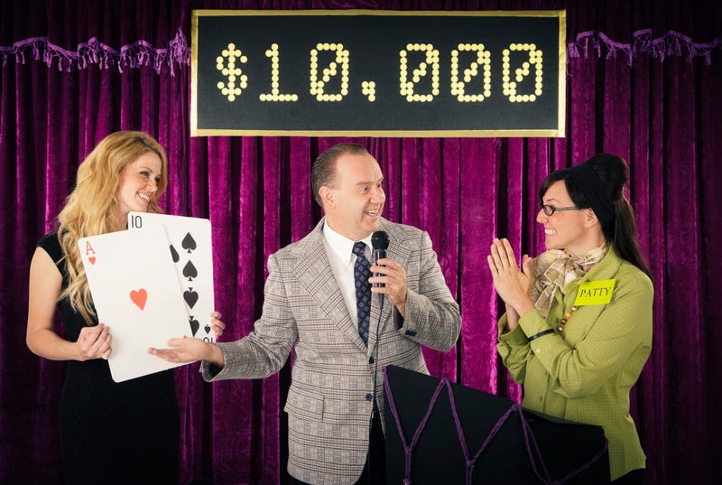 An old fashioned game show host holding a microphone standing with the contestant and assistant.