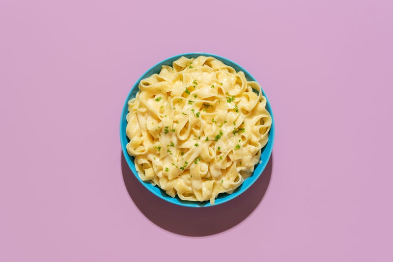 Top view with a pasta alfredo dish minimalist on a purple-colored table. Delicious fettuccine pasta with parmesan and butter, Italian recipe.