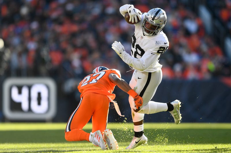 Josh Jacobs #28 of the Las Vegas Raiders runs with the ball as Damarri Mathis #27 of the Denver Broncos works to make a tackle in the first quarter at Empower Field At Mile High on November 20, 2022 