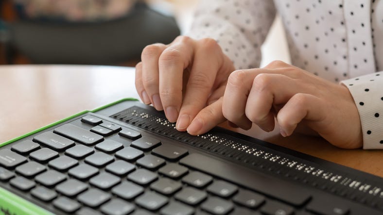 A blind woman uses a computer with a Braille display and a computer keyboard