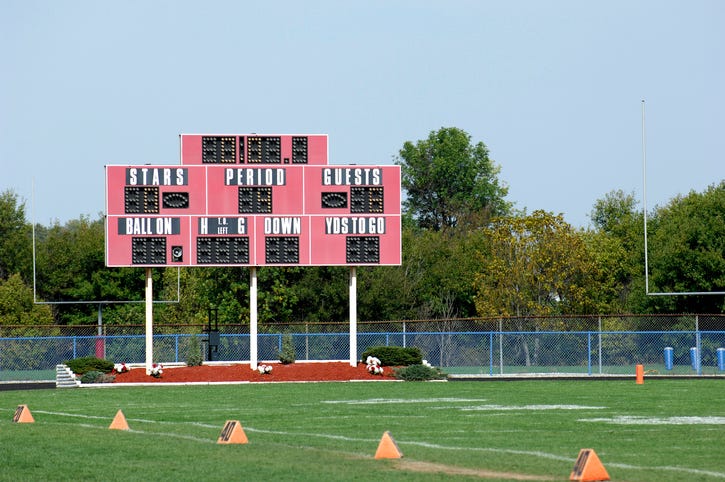 A football field. Focus is on the scoreboard. The cross posts are visible in the background.