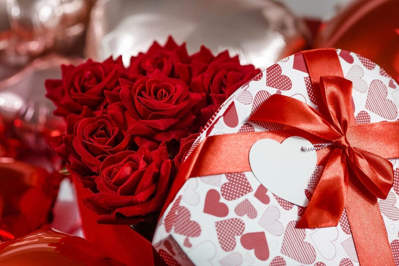 Valentine's day. Red roses in a white box in the form of a heart on the background of foil balls. A gift for women on a holiday. The concept of delivering flowers. floristry and flower shops. - stock photo