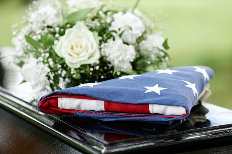 A folded American flag and flowers on top of a casket.