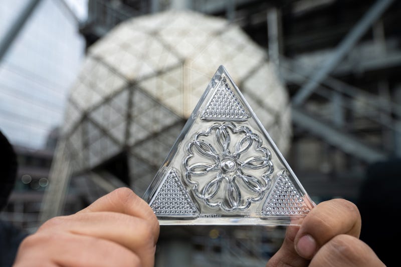 This year’s “Gift of Love” crystal design is “represented by a circle of overlapping hearts entwined together.” A worker holds up one of the crystal triangles as the ball is installed on Dec. 27, 2022