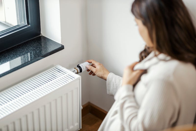 Woman fussing with heating unit inside apartment.