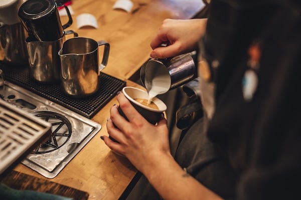 Barista pouring milk to make a cup of cappuccino coffee in a coffee shop