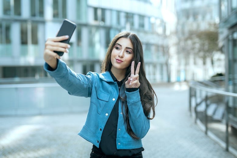 Teenage girl holding a peace sign taking a selfie