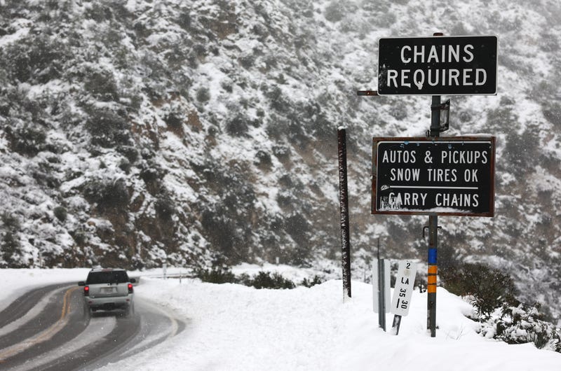 LA CANADA FLINTRIDGE, CALIFORNIA - FEBRUARY 24: A vehicle drives past a 'chains required' sign amid snowfall along a roadway in Los Angeles County, in the San Gabriel Mountains in Angeles National Forest, on February 24, 2023 near La Canada Flintridge, California.