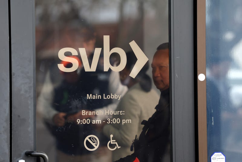 A security guard at Silicon Valley Bank monitors a line of people outside the office on March 13, 2023 in Santa Clara, California. Days after Silicon Valley Bank collapsed, customers are lining up to try and retrieve their funds from the failed bank.