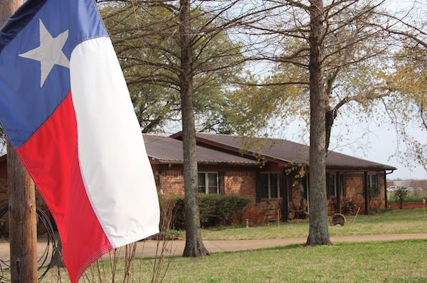 Texas flag with a brick ranch house in the background
