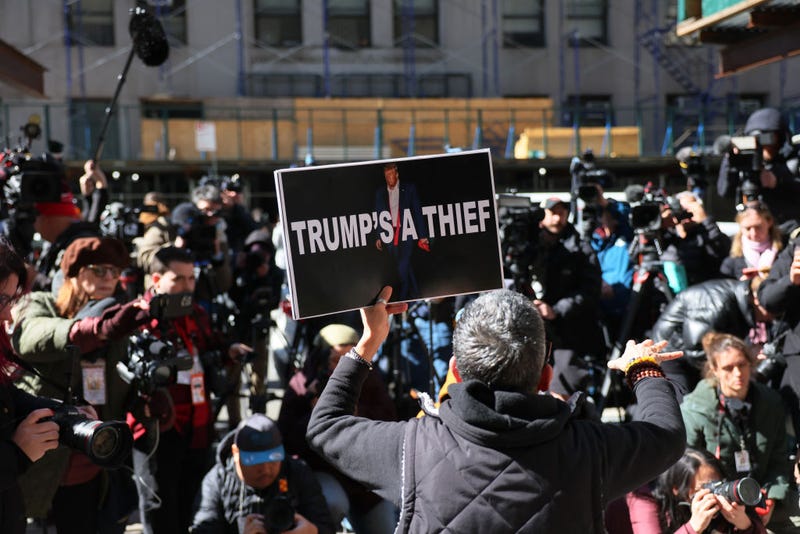 A person holds up a protest sign in front of journalists outside of Louis J. Lefkowitz State Office Building on March 20, 2023 in New York City.
