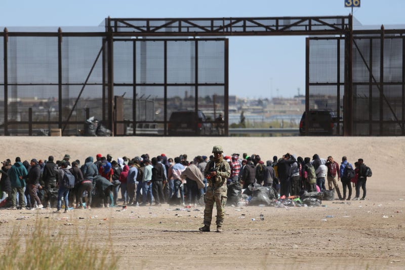 Migrants who crossed the border trough the Rio Bravo from Mexico into the U.S. wait next to the U.S. border wall where U.S. Border Patrol agents stand guard on March 30, 2023 in Ciudad Juarez, Mexico.