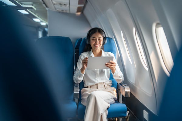 Smiling woman wearing headphones, working on a tablet during a flight