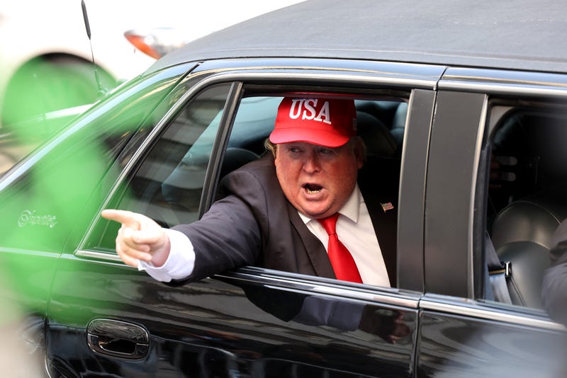 A person dressed as former President Donald Trump rides in a car past Trump Tower on April 04, 2023