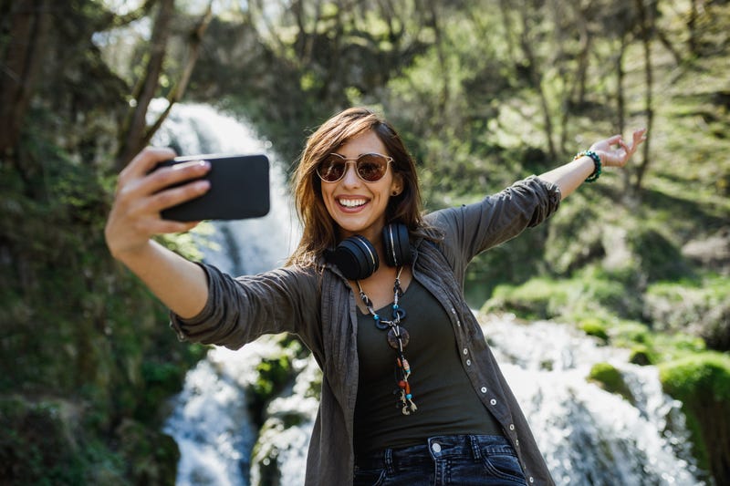 A young woman taking selfie at a waterfall. 