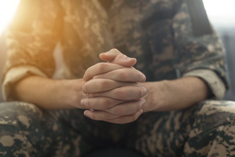 A person in a military uniform joining their hands together.