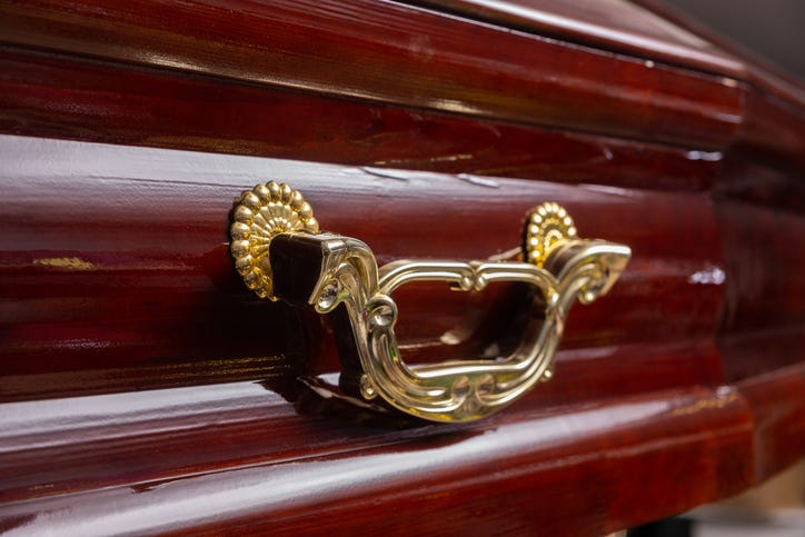 Closeup shot of a funeral casket or coffin in a spicialized shop. The coffin is made of mahogany with yellow metal fittings.