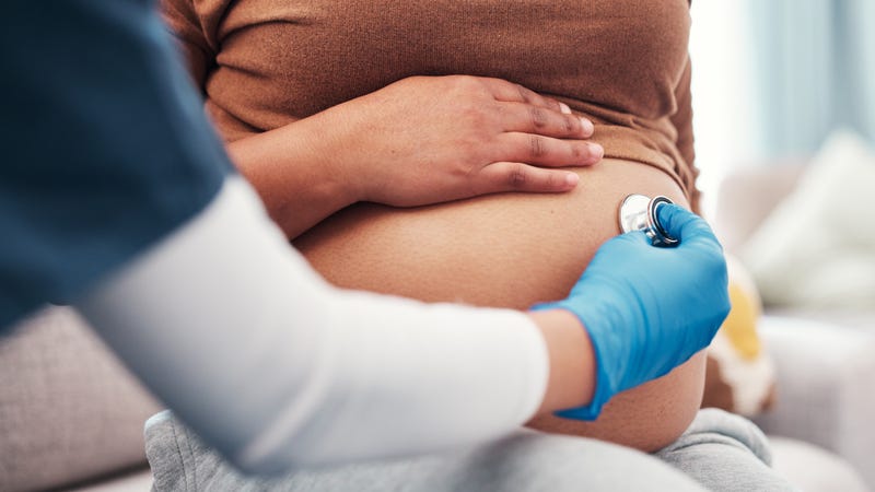 Closeup of a doctor placing a stethoscope on a woman's pregnant stomach