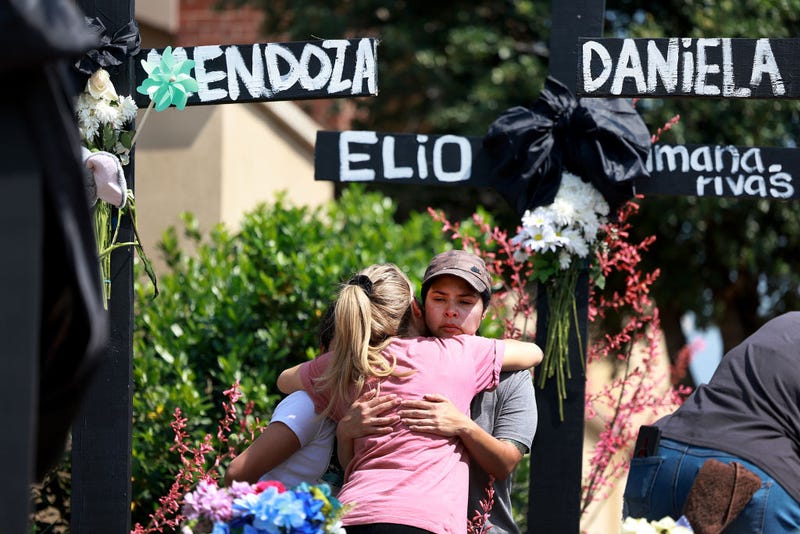 A mother (who didn't want to provide her name) (R) is comforted as she visits a cross that bears the name of one of her children's best friends at the memorial set up near the scene of a mass shooting at the Allen Premium Outlets mall on May 9, 2023 in Allen, Texas. Eight people were killed and seven wounded in the attack on Saturday. The gunman was killed at the scene by an Allen Police officer responding to an unrelated call. Three of the wounded are in critical condition, according to reports. (Photo by Joe Raedle/Getty Images)