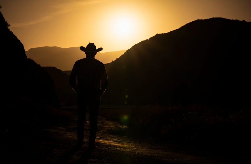 Silhouette of adult man in cowboy hat against mountain and sky during sunset