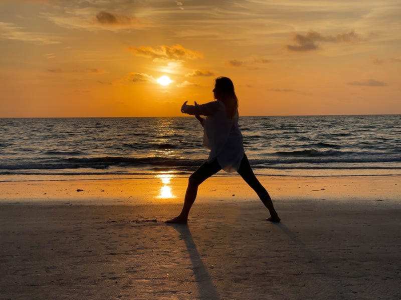 Profile view of senior woman as she stands exercising with Tai Chi against water, sky and clouds on gulf coast Florida beach