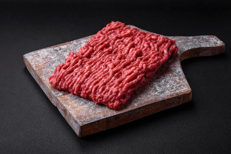 Raw ground beef or pork on a wooden cutting board with spices and salt on a dark concrete background
