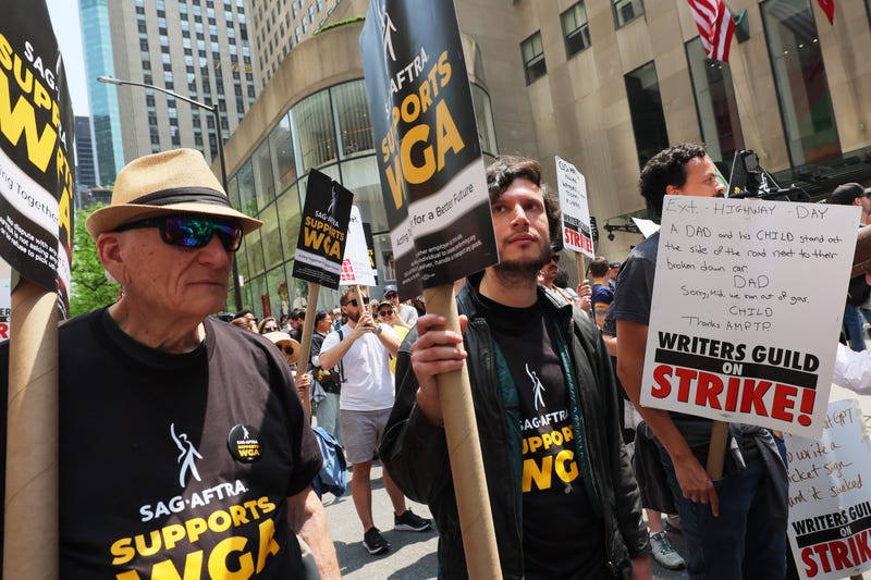 people with picket signs that say sag-aftra supports wga