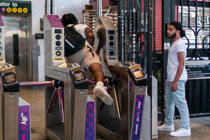 A man goes over a subway turnstile without paying the MTA fare as other wait for him to open the door at a subway station in middle Manhattan on June 5, 2023