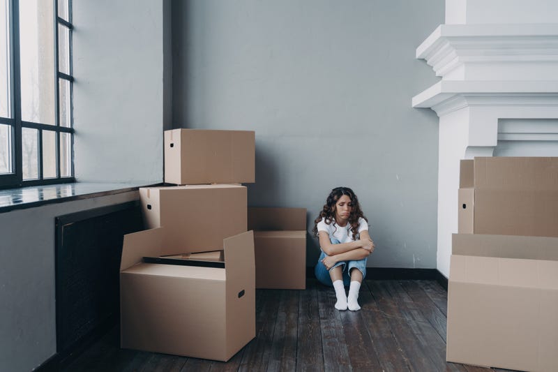 Sad woman sitting amidst packed boxes in empty room, feeling despair. Overwhelmed by divorce or eviction.