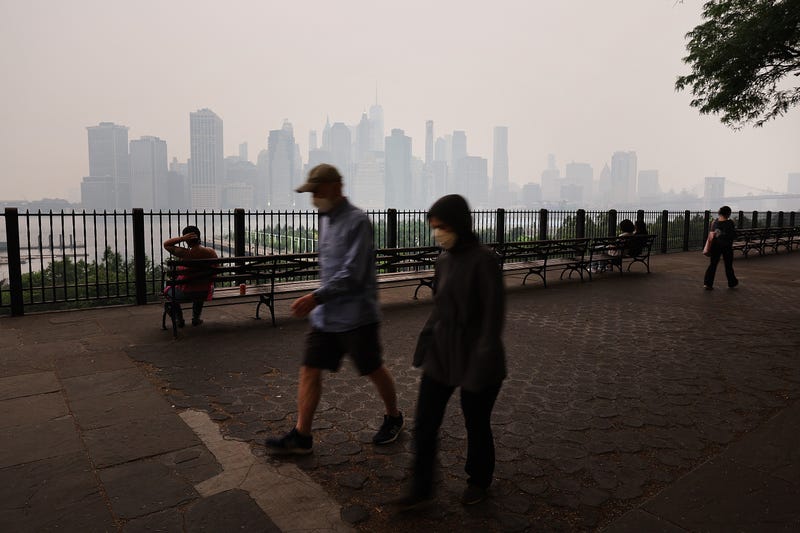 People walk along the Brooklyn Promenade as a reddish haze enshrouds the Manhattan skyline as a result of Canadian wildfires on June 6, 2023, in New York City