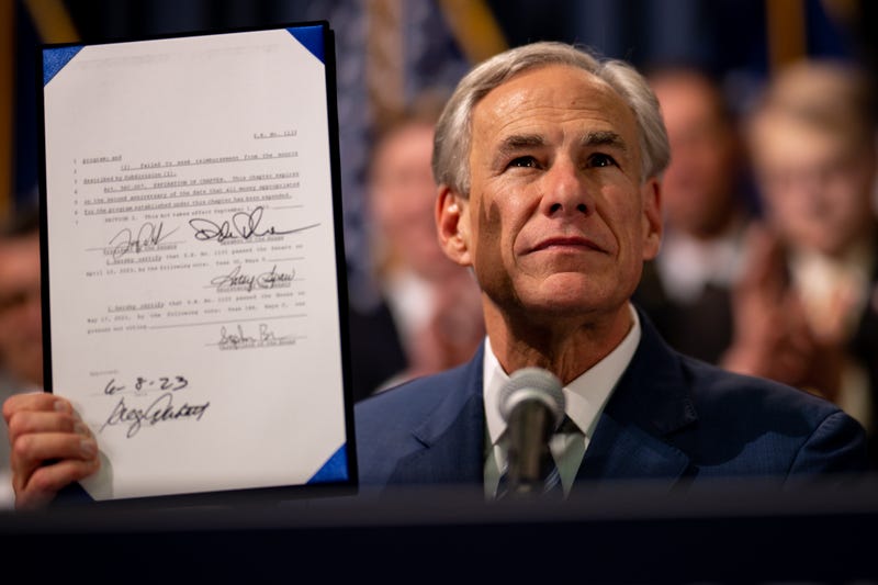 greg abbott holding up a bill