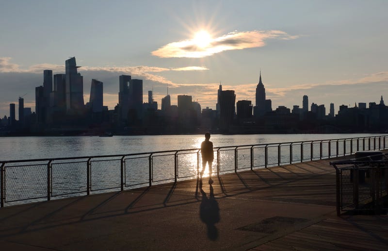 The sun rises behind the skyline of Midtown Manhattan as a person walks on a pier by the Hudson River on June 9, 2023, in Hoboken, New Jersey