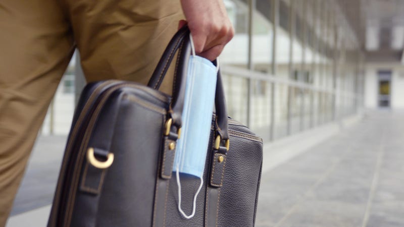 Cropped shot of businessman holding briefcase and safety mask walking outdoors. Close up of male carry leather bag and protective mask walk outside building.