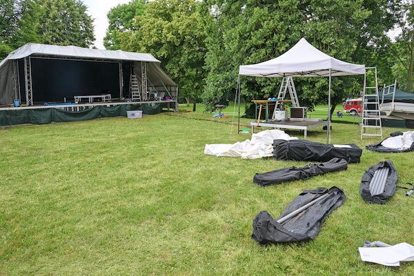 Open air stage, pavilion for the sound system, tent poles and canvas in bags for setting up a music festival on the green meadow in the park