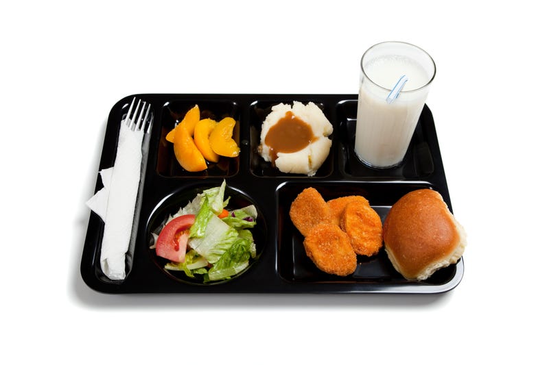 A black school lunch tray including tossed salad, chicken nuggets, roll, peaches, mashed potatoes and gravy with milk on a white background