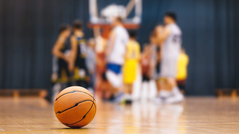 People playing basketball in soft focus, with a basketball in the foreground