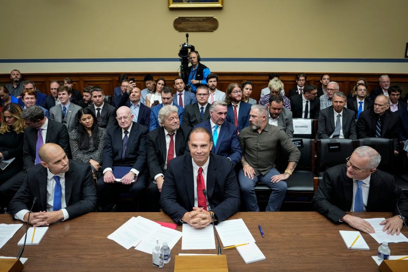 three men sit at panel in house committee room with a crowd in the seats behind them