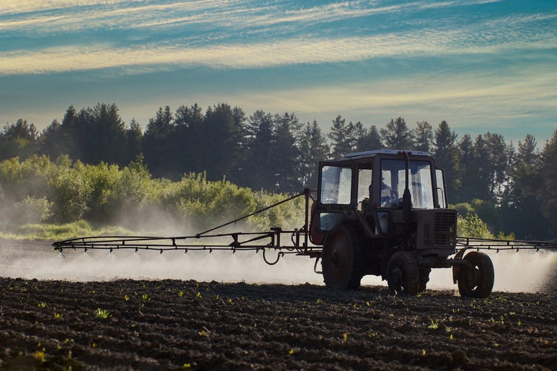 An aerosol cloud behind farm tractor spraying herbicides in potato field.